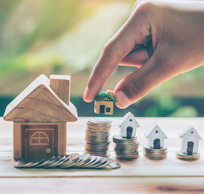 Small houses on top of increasingly tall stacks of coins lead to a larger house at the end of the row of coin stacks. The stacks go from smallest on the right to largest on the left.